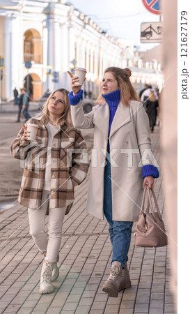 two young girls are walking along the city street, drinking coffee, talking two young girls are walking along the city street, drinking coffee, talking 121627179
