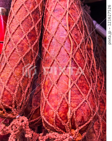 Vividly colored sausages hang in a market, showcasing intricate netting 121627526