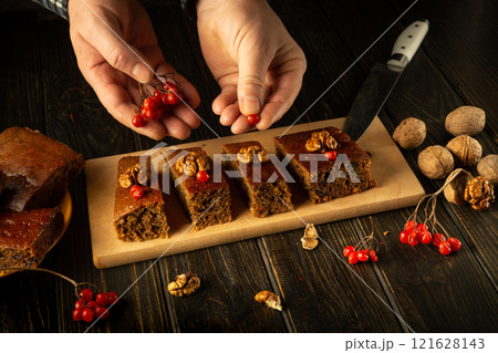 Hands gently place vibrant red berries above rich, moist squares on a wooden platter. The setting is warm and inviting, showcasing a delightful array of homemade pastries Hands gently place vibrant red berries above rich, moist squares on a wooden platter. The setting is warm and inviting, showcasing a delightful array of homemade pastries 121628143