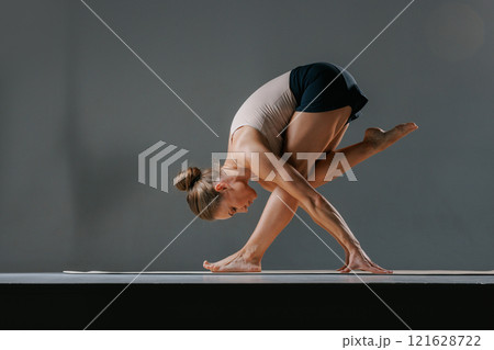 An athletic young woman performs the stretching pose Baddha Parsvakonasana, or Bound Side Angle Pose, during her daily yoga practice at a studio. 121628722