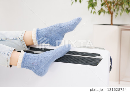 Young woman in warm winter socks near electric heater. Concept of heating season. 121628724