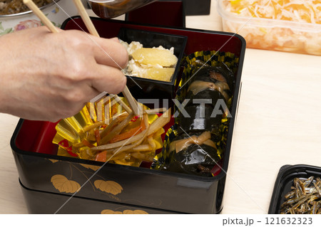 おせち料理を箸で重箱に詰める　 121632323
