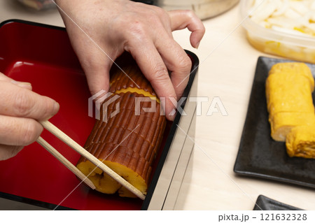 おせち料理を箸で重箱に詰める　 121632328