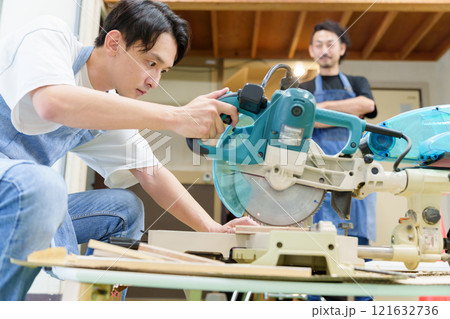 電動ノコギリを使う職人と弟子 121632736