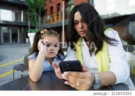 Mother and daughter enjoying time together while looking at a phone outside a modern building on a sunny day Mother and daughter enjoying time together while looking at a phone outside a modern building on a sunny day 121633383