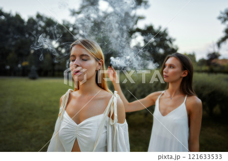 Women engage in ritual with smoke in serene outdoor setting at twilight 121633533