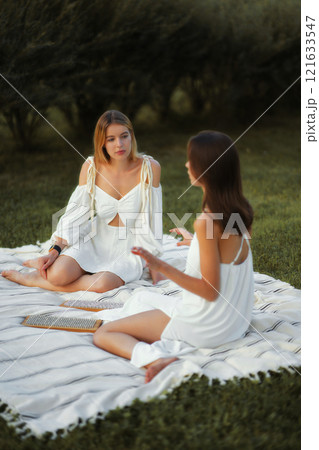 Two women enjoying a conversation on a blanket in a garden during the afternoon Two women enjoying a conversation on a blanket in a garden during the afternoon 121633547