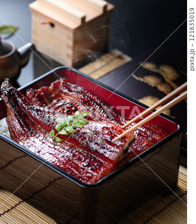 湯気立つうな重を箸で持ち上げたシズル感あふれる和食カット 121635019
