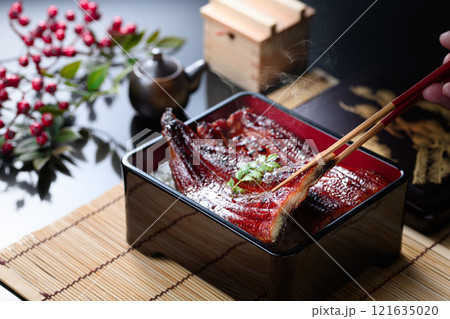湯気立つうな重を箸で持ち上げたシズル感あふれる和食カット 湯気立つうな重を箸で持ち上げたシズル感あふれる和食カット 121635020