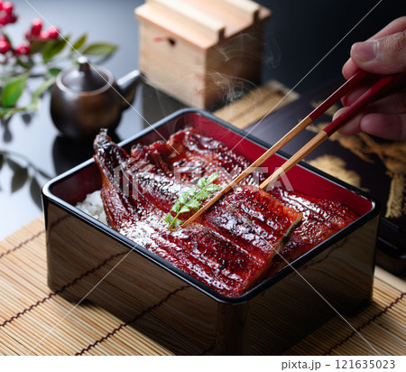 湯気立つうな重を箸で持ち上げたシズル感あふれる和食カット 121635023