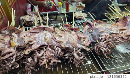 Freshly grilled barbecue squid on skewers displayed at an Asian street food market showcasing vibrant culinary traditions 121636352