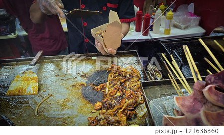 Freshly grilled barbecue squid on skewers displayed at an Asian street food market showcasing vibrant culinary traditions 121636360