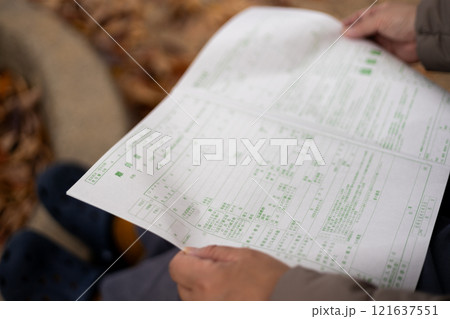 公園のベンチに座り込み、離婚届を眺める中高年女性 121637551