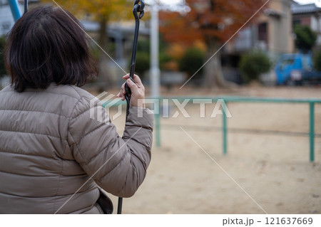 人のいない公園で一人ブランコに乗る中高年女性の後ろ姿 人のいない公園で一人ブランコに乗る中高年女性の後ろ姿 121637669