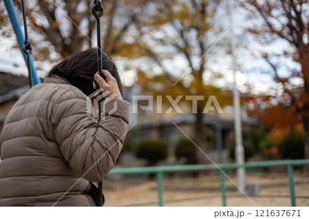 人のいない公園で一人ブランコに乗る中高年女性の後ろ姿 121637671