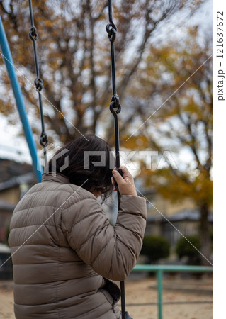 人のいない公園で一人ブランコに乗る中高年女性の後ろ姿 人のいない公園で一人ブランコに乗る中高年女性の後ろ姿 121637672
