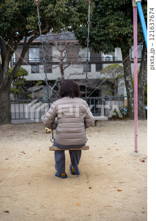 人のいない公園で一人ブランコに乗る中高年女性の後ろ姿 121637674