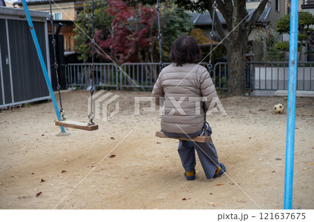 人のいない公園で一人ブランコに乗る中高年女性の後ろ姿 121637675
