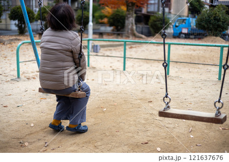 人のいない公園で一人ブランコに乗る中高年女性の後ろ姿 121637676
