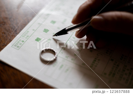 結婚指輪を外して離婚届に記入しようとしている中高年女性の手元 結婚指輪を外して離婚届に記入しようとしている中高年女性の手元 121637888