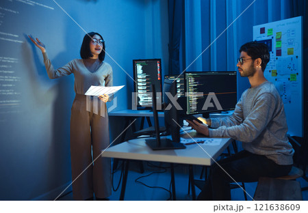 asian woman developers collaborating on a coding project, with one member presentation at code projected on the wall while the other works on multiple computer screens asian woman developers collaborating on a coding project, with one member presentation at code projected on the wall while the other works on multiple computer screens 121638609