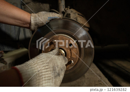 Car repairs. A man unscrews the bolts on a car wheel hub to replace a ball joint. A man wearing work gloves independently replaces a ball joint in a car in his garage. 121639282