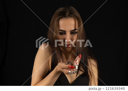 For halloween, the witch holds a ring in her hand and reads a spell on a black background. Beautiful female gothic witch stares at the ring in her hand. Halloween and witchcraft concept. For halloween, the witch holds a ring in her hand and reads a spell on a black background. Beautiful female gothic witch stares at the ring in her hand. Halloween and witchcraft concept. 121639340
