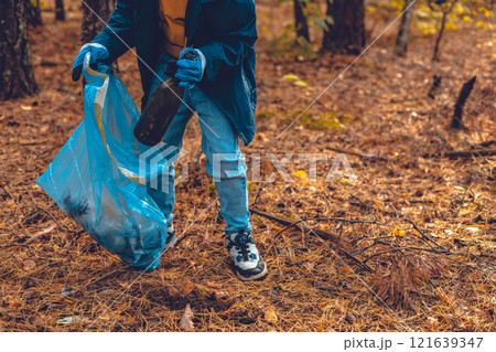 A child volunteer collects plastic waste in a garbage bag. A child eco activist saves the forest from plastic waste. Pollution of the planet with garbage, environmental problems. 121639347