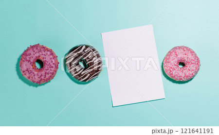 A festive flat lay featuring vibrant donuts with colorful toppings and a blank greeting card on a pink background A festive flat lay featuring vibrant donuts with colorful toppings and a blank greeting card on a pink background 121641191
