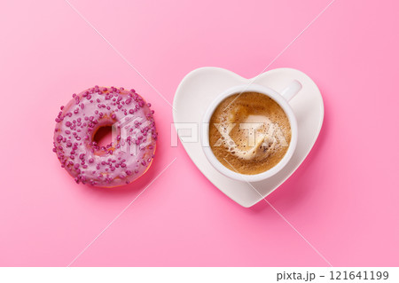 A vibrant donut and a coffee cup on a heart-shaped saucer, perfect for a Valentines Day card 121641199