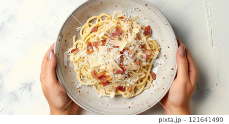 Top view of beautiful female hands holding plate with spaghetti carbonara with grated parmesan cheese and bacon on white background, concept of national Italian cuisine 121641490