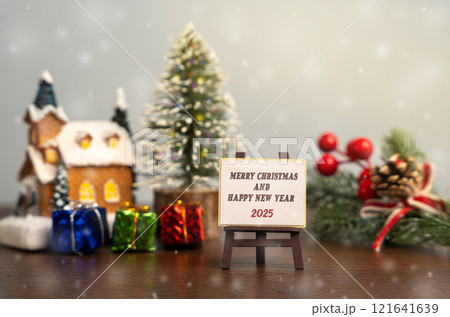 Easel Merry Christmas and Happy New Year 2025. Xmas winter holiday. Decoration, celebration. The concept of the beginning of the new year. Christmas tree, gifts and a house with snowfall 121641639