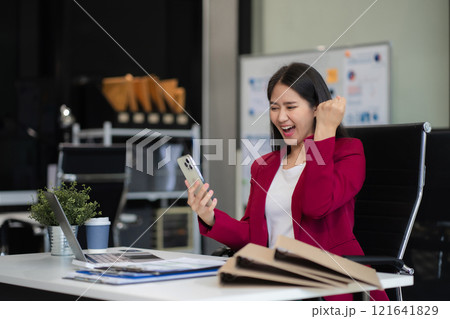 Businessman using smartphone and laptop computer in office. Happy woman, entrepreneur, small business owner working online. Businessman using smartphone and laptop computer in office. Happy woman, entrepreneur, small business owner working online. 121641829