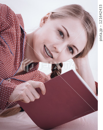 Woman relaxing in bed reading book 121642433