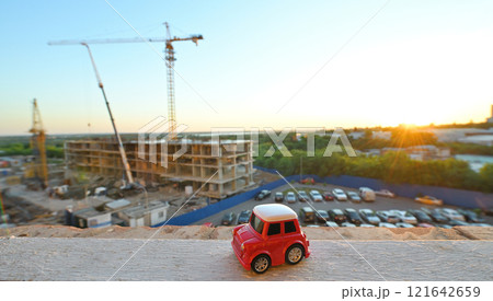 a small red toy car against the backdrop of a house under construction and sunset. 121642659