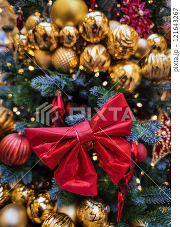 Beautifully decorated Christmas tree adorned with gold ornaments and a large red bow in a festive setting during holiday season Beautifully decorated Christmas tree adorned with gold ornaments and a large red bow in a festive setting during holiday season 121643267