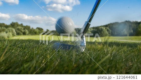 Golf club hits a golf ball. Drops of morning dew and grass particles rise into the air after the impact. Golf club hits a golf ball. Drops of morning dew and grass particles rise into the air after the impact. 121644061