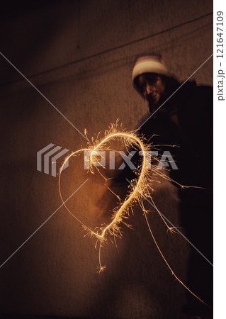 Girl painting heart with freeze light. Heart shape with festive freezing lights in the night. Sparkling heart made by fire. Stop light drawings. Love concept. Saint Valentines surprise.  121647109
