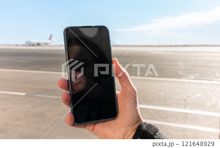Girl holds a smartphone with a black screen close-up. Phone on the background of the airport with an airplane Girl holds a smartphone with a black screen close-up. Phone on the background of the airport with an airplane 121648929