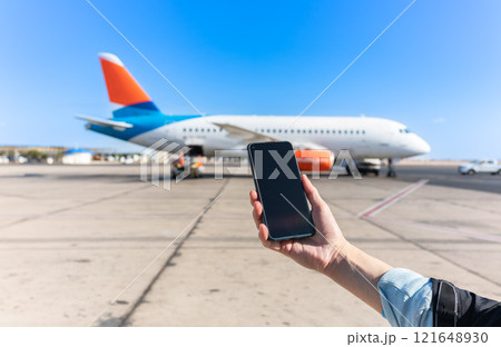 Girl holds a smartphone with a black screen close-up. Phone on the background of the airport with an airplane Girl holds a smartphone with a black screen close-up. Phone on the background of the airport with an airplane 121648930