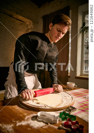 Close up portrait of man, dressed superhero costume, carefully pressing dough with rolling pin, immersing in peaceful routine. 121649862
