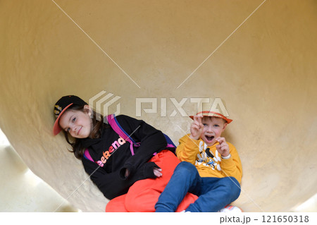 A boy and a girl happily sit on a slide in winter wearing helmets. They enjoy the leisure event, surrounded by a beautiful landscape, having fun and relaxing A boy and a girl happily sit on a slide in winter wearing helmets. They enjoy the leisure event, surrounded by a beautiful landscape, having fun and relaxing 121650318