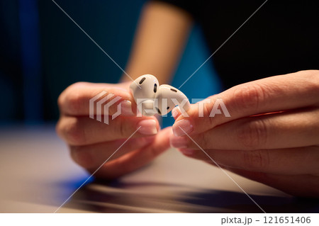 Closeup image of a person holding a pair of wireless earbuds firmly in their hands 121651406