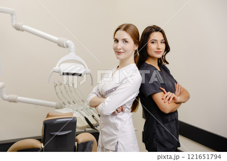Smiling dentist and assistant with crossed hands looking at the camera in dental clinic Smiling dentist and assistant with crossed hands looking at the camera in dental clinic 121651794
