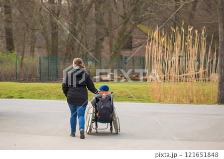Woman walking in the park with a boy sitting in a wheelchair Woman walking in the park with a boy sitting in a wheelchair 121651848