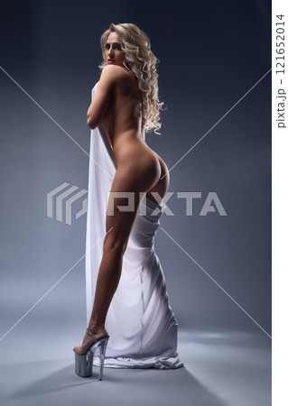 Athletic naked woman wearing white fabric in studio and looking into camera 121652014