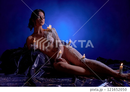 Naked slim woman with burning candles in her hands looking away in antique room Naked slim woman with burning candles in her hands looking away in antique room 121652050