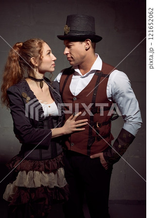 Loving couple in vintage outfits looking at each other against grey background 121652062