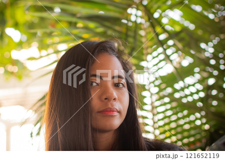 portrait of a beautiful Filipina woman against a background of palm leaves in the rays of the sun portrait of a beautiful Filipina woman against a background of palm leaves in the rays of the sun 121652119