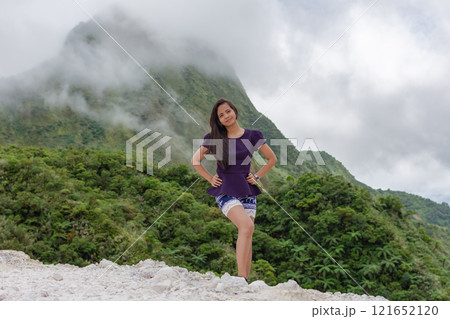 Portrait of a beautiful young Filipina woman against the background of a volcano covered with smog and clouds 121652120